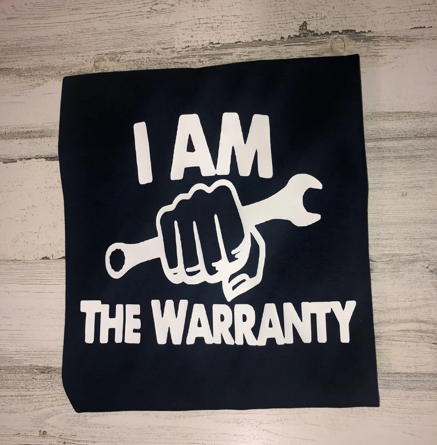A navy shirt she made, white vinyl lettering reading I AM THE WARRANTY around a fist and wrench.